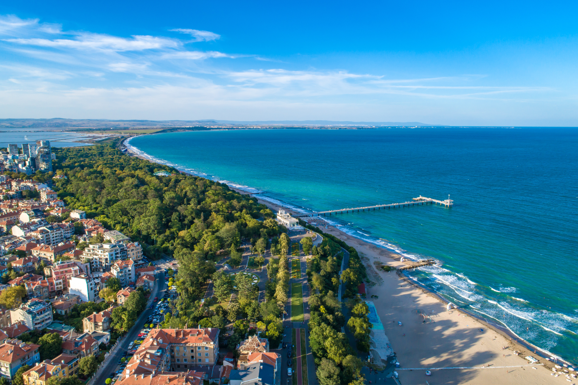 Luchtfoto van een kustplaats met strand en een pier aan de blauwe zee.